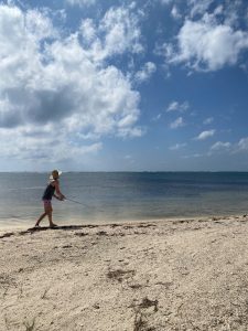 Fly angler presenting a fly to bonefish along a calm beach flat in Grand Cayman, Cayman Islands