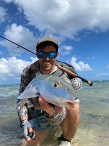 Fly angler wading in shallow water holding a freshly caught bonefish on the flats in Grand Cayman, Cayman Islands
