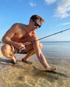 Fly angler releasing a bonefish in clear, shallow water during a calm morning in Grand Cayman, Cayman Islands