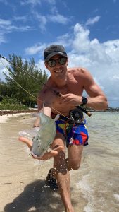 Happy fly angler holding a bonefish caught sight fishing on foot in shallow water along a beach in Grand Cayman, Cayman Islands