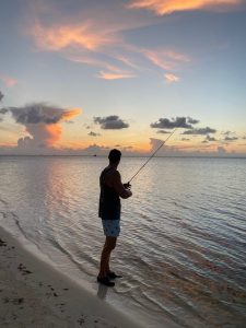 Angler fly fishing from the beach at sunset on a calm evening in Grand Cayman, Cayman Islands