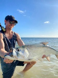 Angler holding a tarpon caught on fly in knee-deep water after a successful shore-based catch in Grand Cayman, Cayman Islands