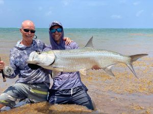 Two anglers posing with a large tarpon caught fly fishing in shallow water with the best local guide in Grand Cayman, Cayman Islands